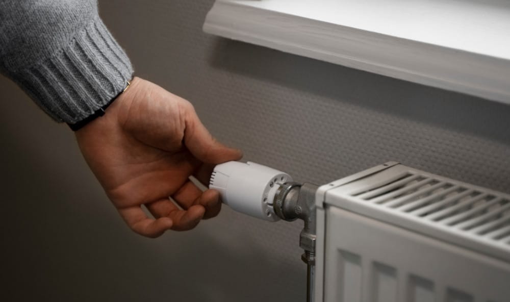 Męska dłoń regulująca termostat przy grzejniku - jak zaoszczędzić na kosztach ogrzewania